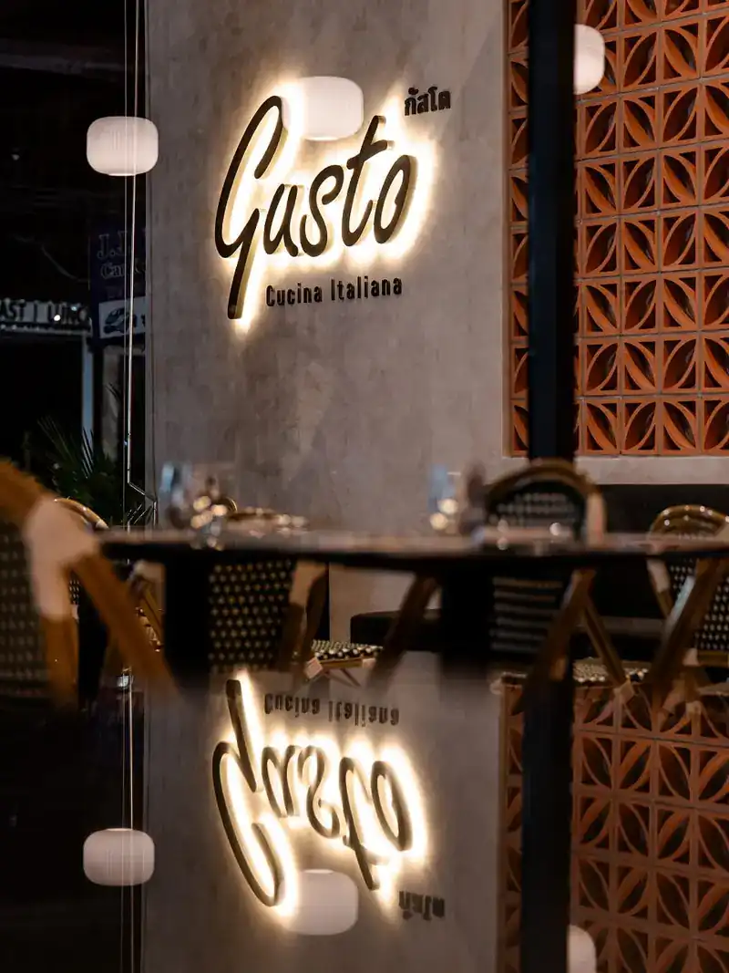 The lit Gusto Cucina Italiana sign reflected in a glass table top