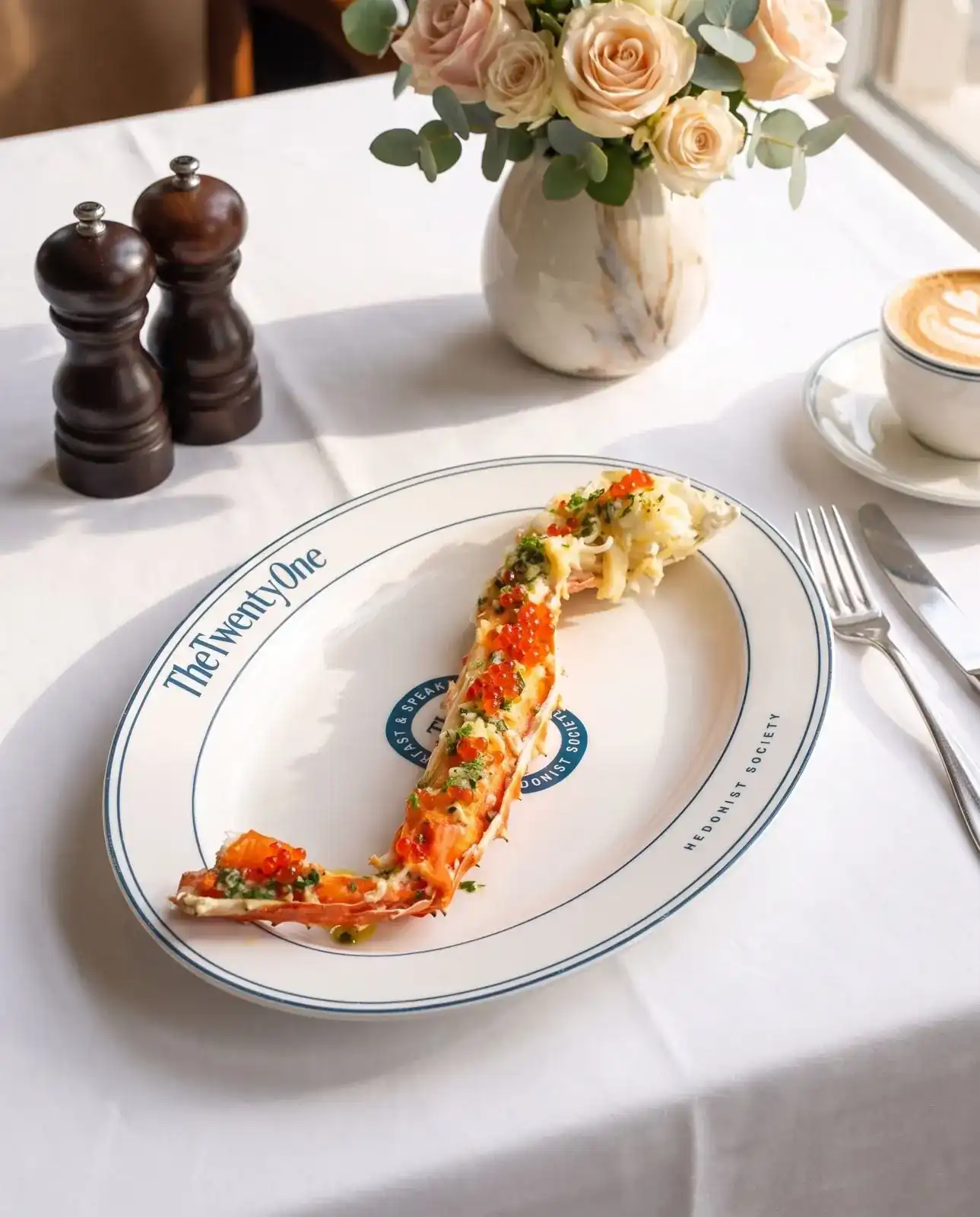 A crab leg dressed with roe and herbs on the restaurant's rimmed oval plate, coffee and roses on white linen