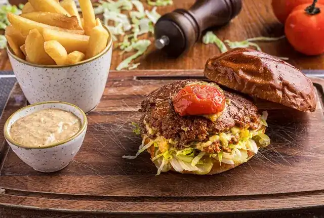A burger on a wooden board with fries and a bowl of sauce