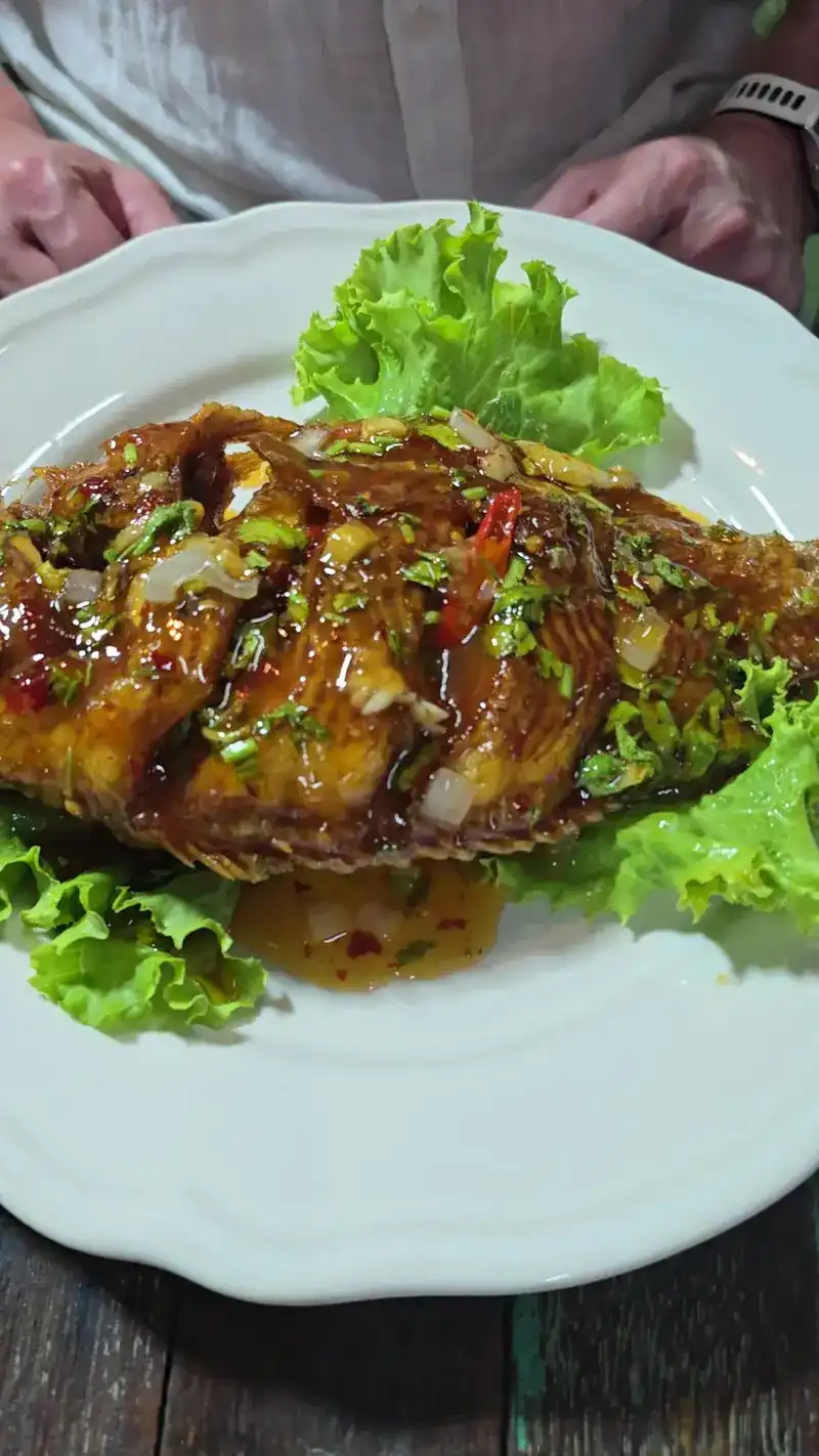A whole fried fish in a glossy chilli sauce on lettuce