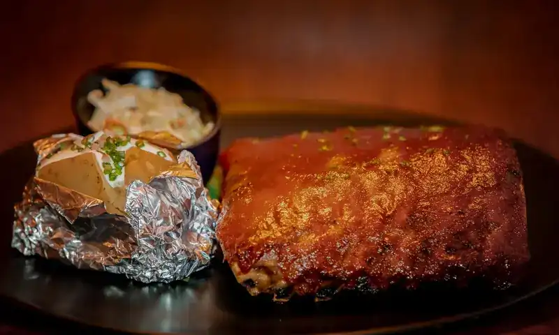 Glazed rack of BBQ back ribs with a baked potato in foil and coleslaw