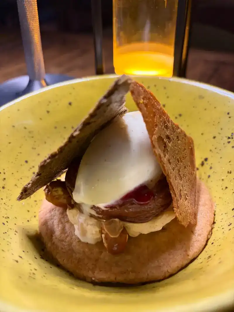 A dessert in a yellow speckled bowl: a white scoop between two thin crisps on a small round cake