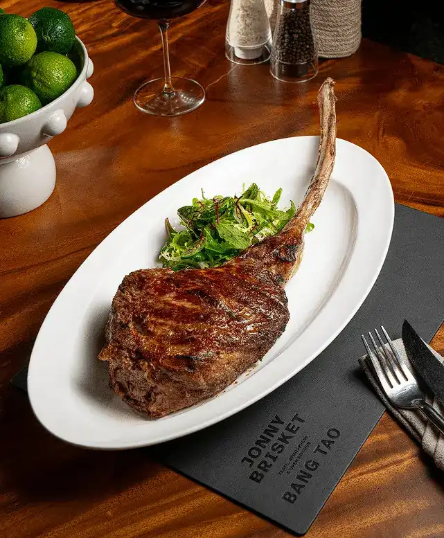 Tomahawk steak with greens on a white plate