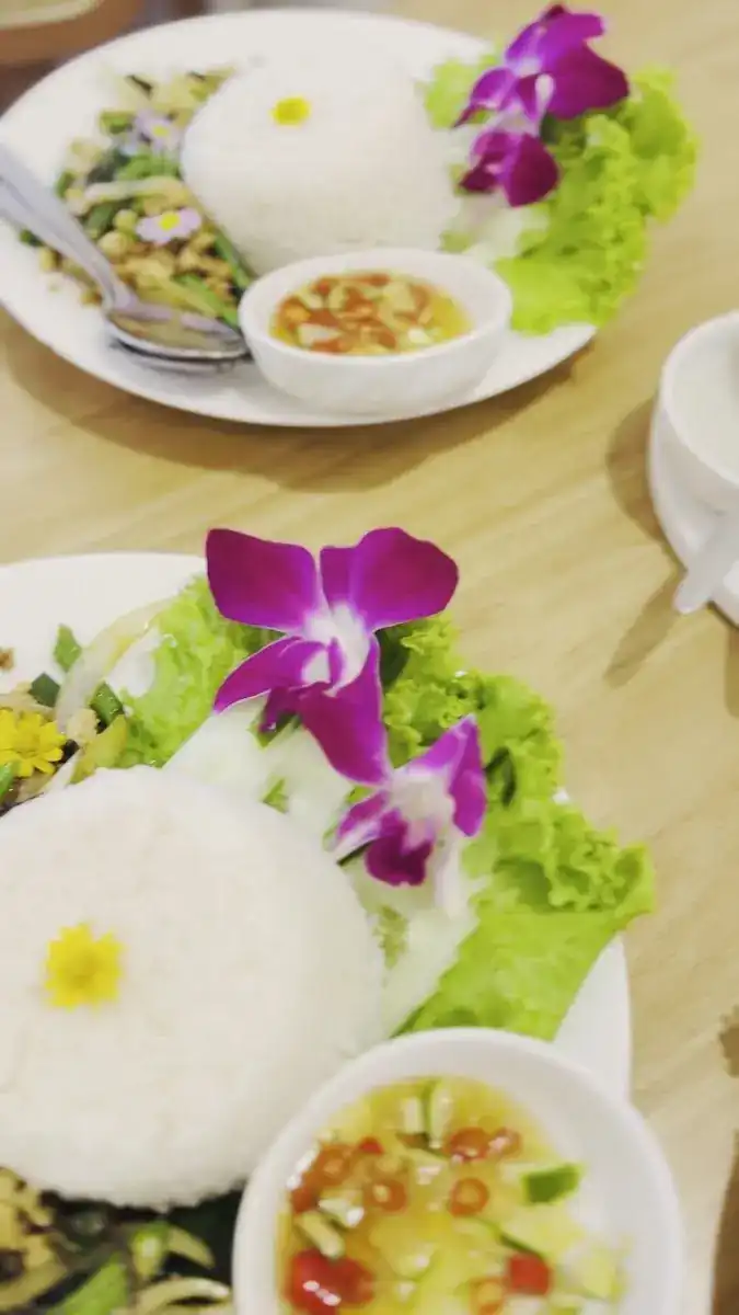 Plates of rice and stir-fry dressed with purple orchids and lettuce, with small bowls of chilli sauce