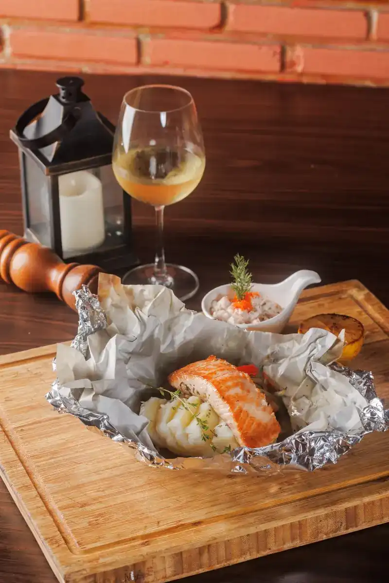 Salmon in foil on a wooden board, a candle lantern and the brick wall behind