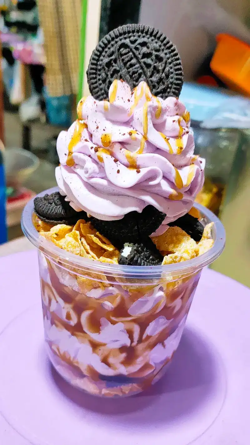 An ice-cream cup with purple whipped cream and chocolate cookies