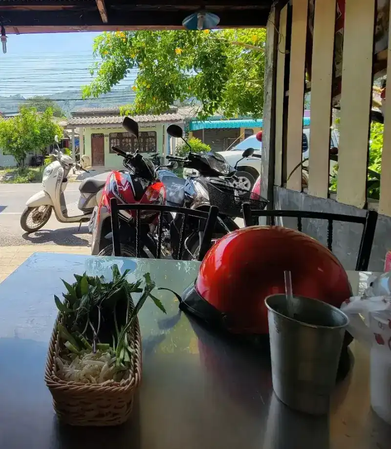 View from a steel table under the shop roof out to the road, with parked scooters, a red helmet and a basket of herbs