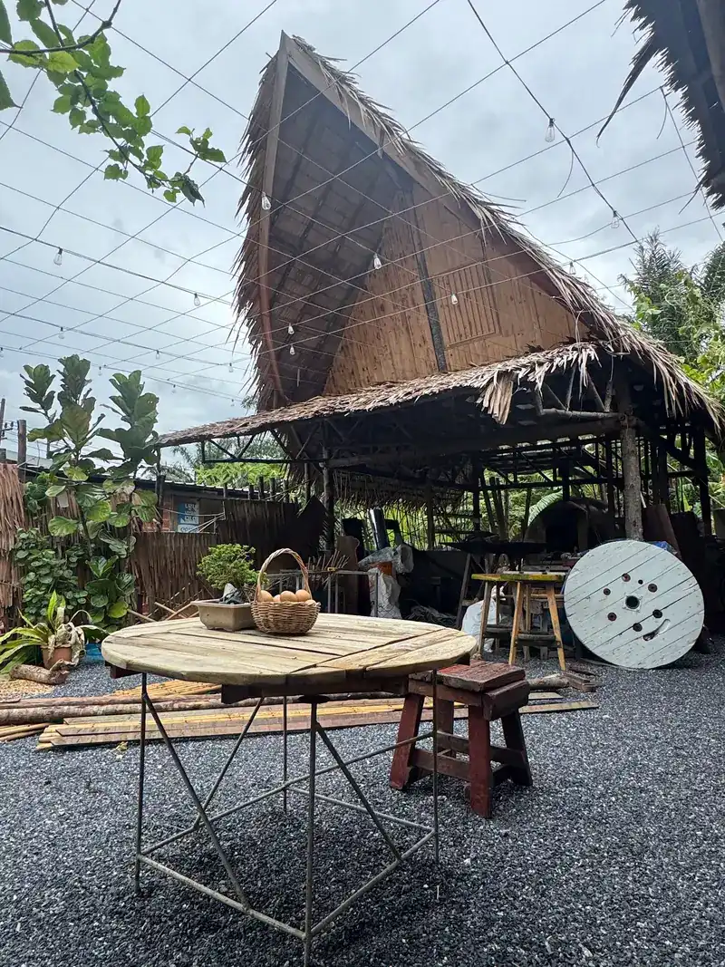 A tall thatched roof over the garden, string lights above and a round wooden table in front