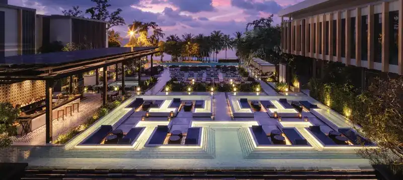 The deck at dusk, with lit lounger islands leading to the palms and the sea