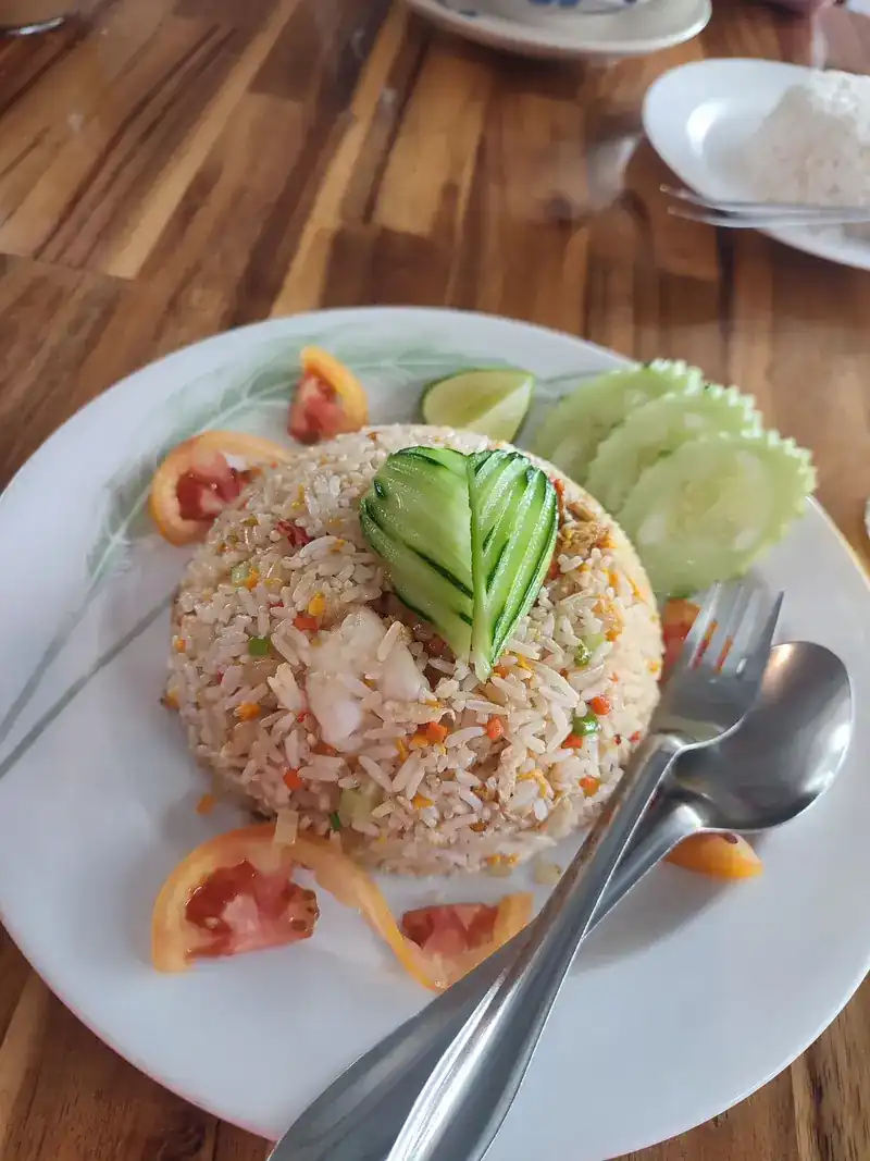 A plate of fried rice with a carved cucumber leaf, tomato and lime