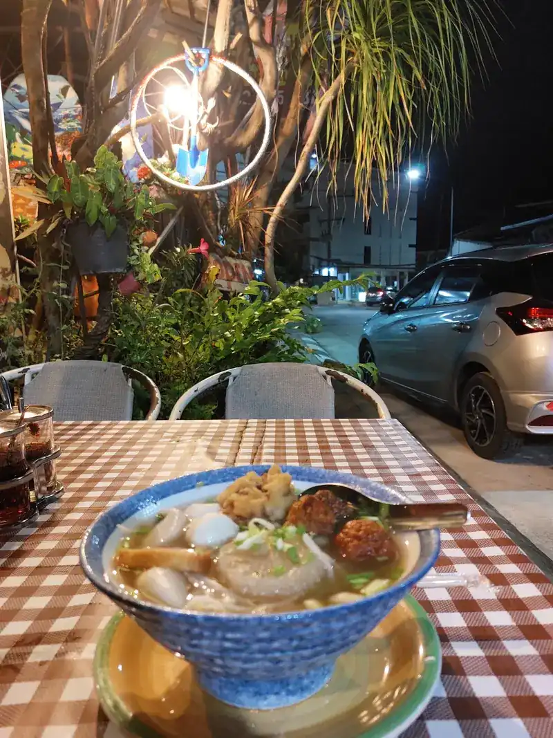 Bowl of noodle soup with meatballs on a checked tablecloth outside at night