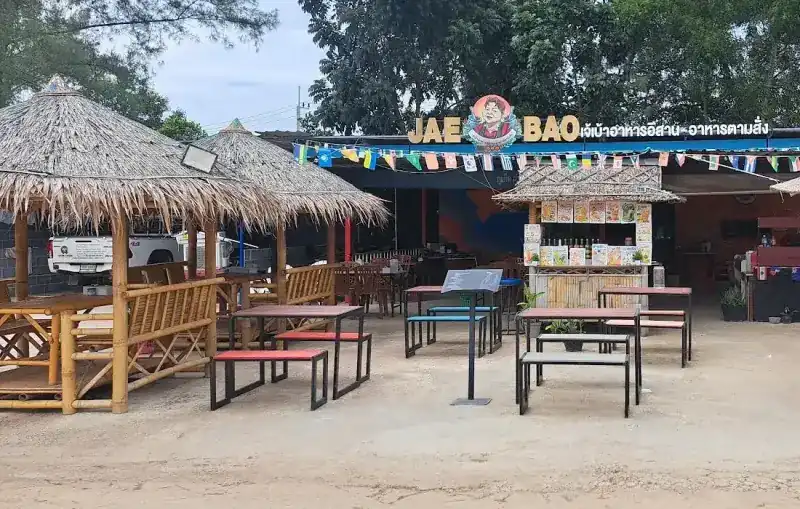 The front of Jae Bao: the JAE BAO sign, bamboo huts with thatched roofs and tables out front