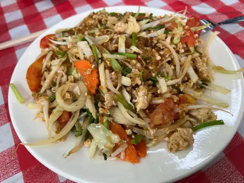 A plate of stir-fried noodles with egg, bean sprouts, carrot and tomato