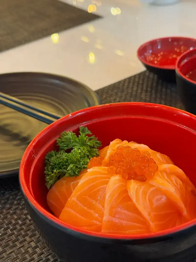 Salmon over rice in a red bowl, topped with salmon roe