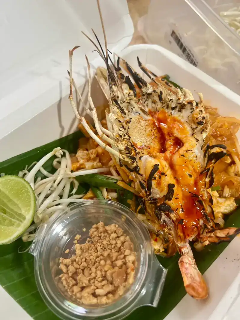 River prawn pad thai in a takeaway box with a cup of crushed peanuts