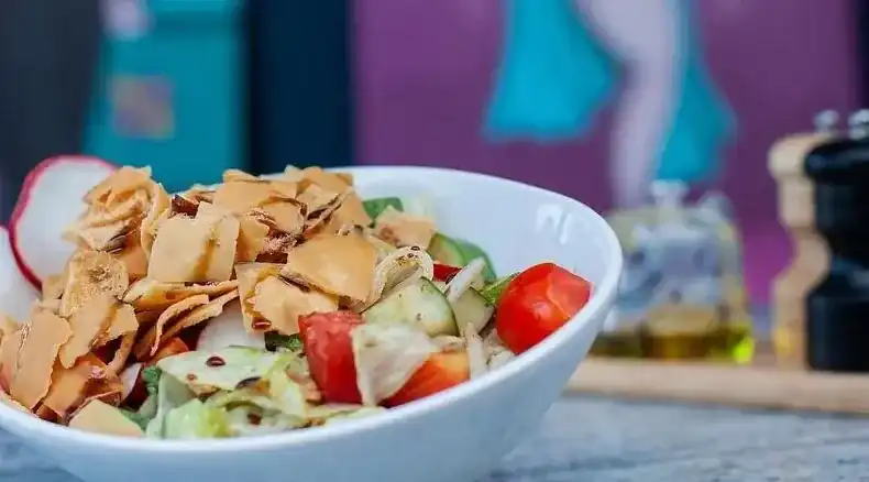 A white bowl of salad piled with crisp fried bread, radish, tomato and cucumber