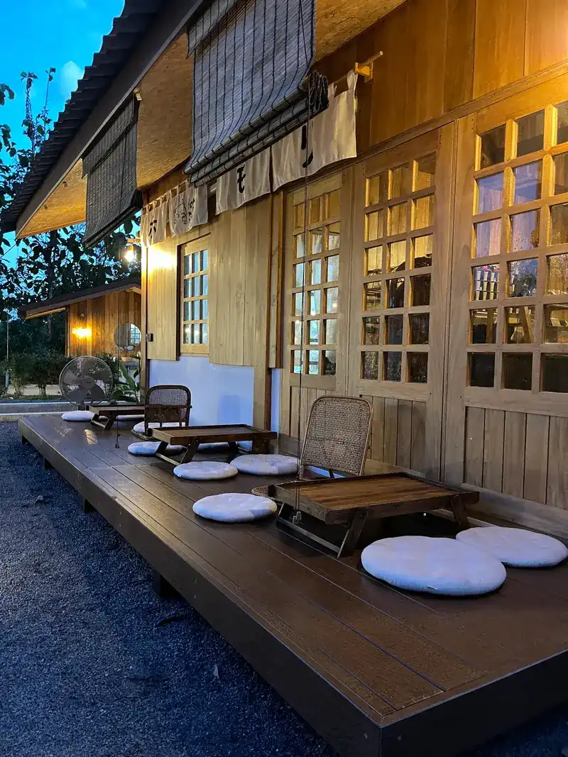 The veranda at dusk: low wooden tables, round floor cushions and lit lattice windows