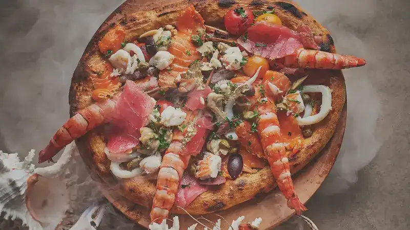 A seafood pizza with prawns, squid and olives on a wooden board