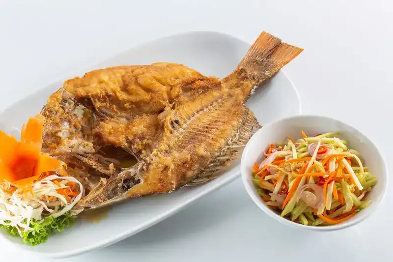 A whole deep-fried fish with a bowl of green mango salad