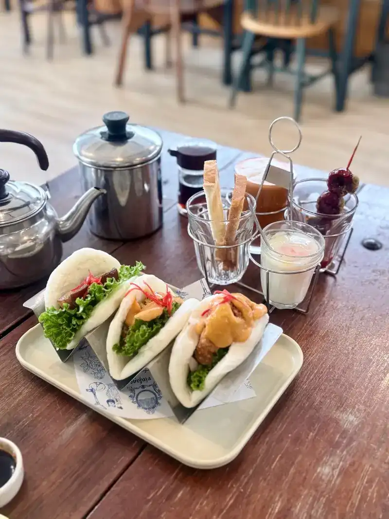 Three filled bao buns on a tray, with a teapot on the wooden table