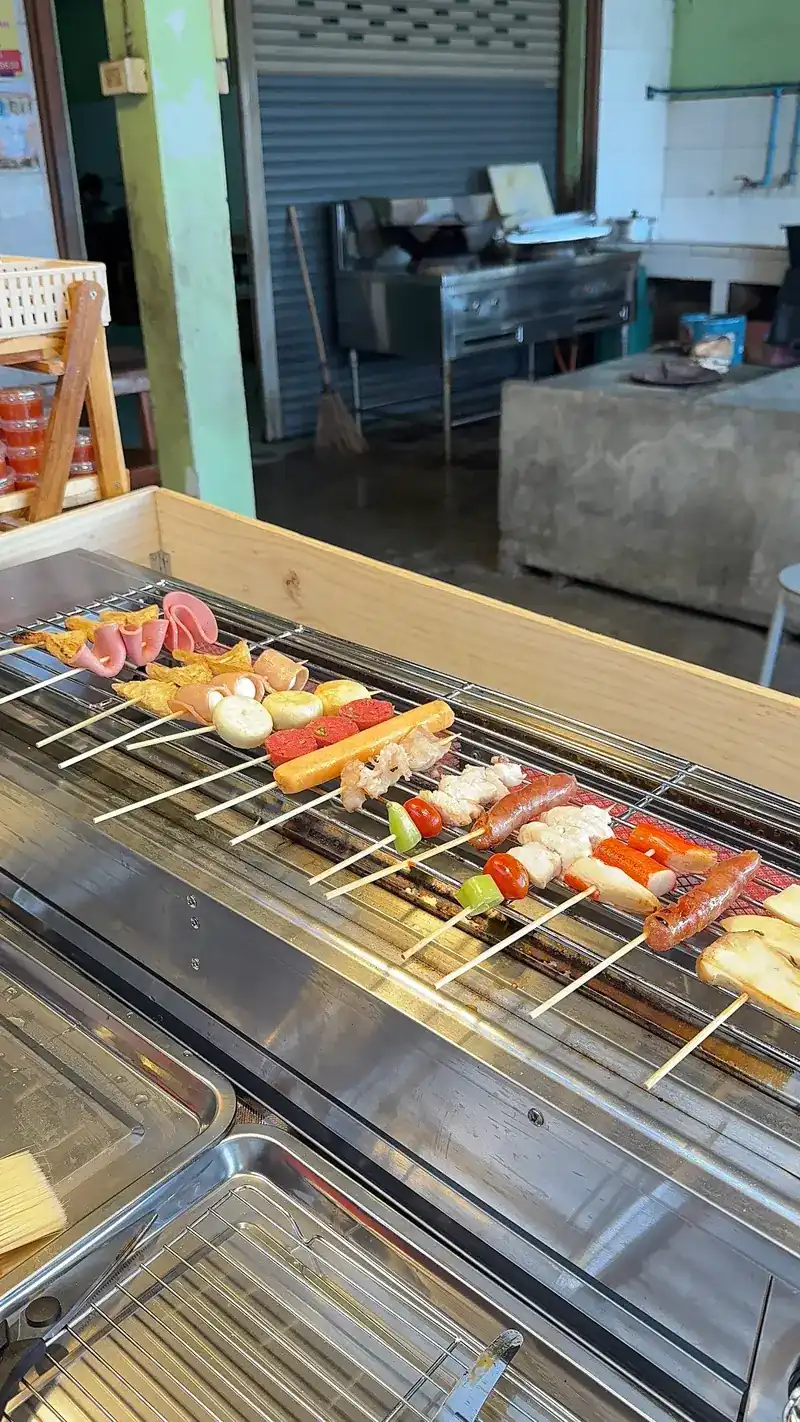Skewers cooking side by side on a long grill