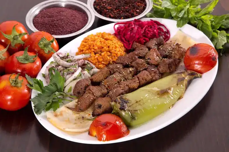 Grilled meat with bulgur pilaf, red cabbage, grilled pepper and tomato, sumac onions and flatbread