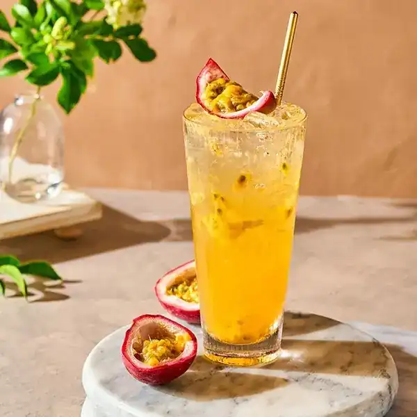 A tall glass of golden tea topped with half a passion fruit