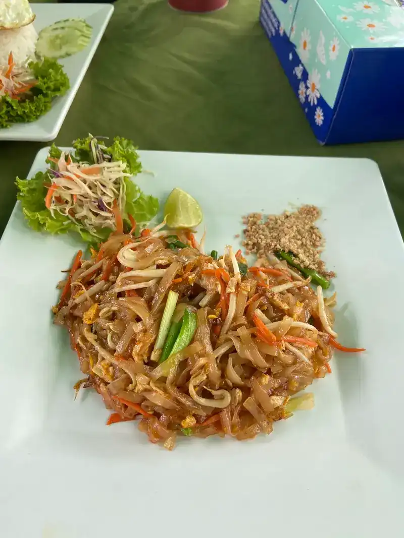 Pad thai with crushed peanuts and a wedge of lime on a white plate