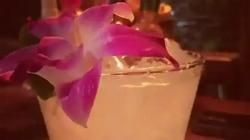 Close view of a pale drink with a purple orchid on the rim